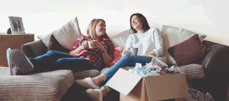 Two women laughing on the sofa with moving boxes