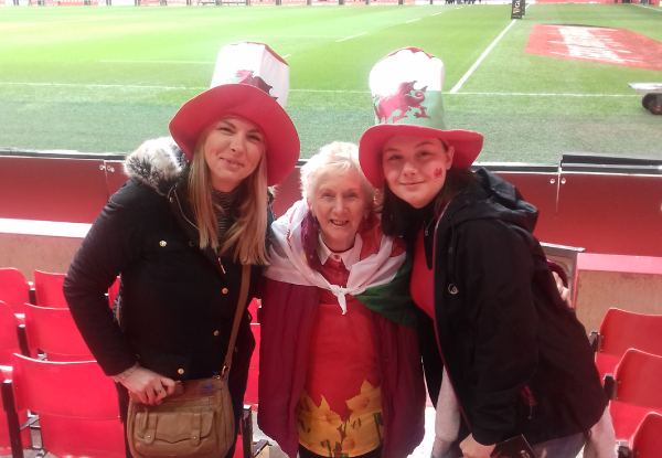 3 women stood in front of rugby pitch with Welsh hats on
