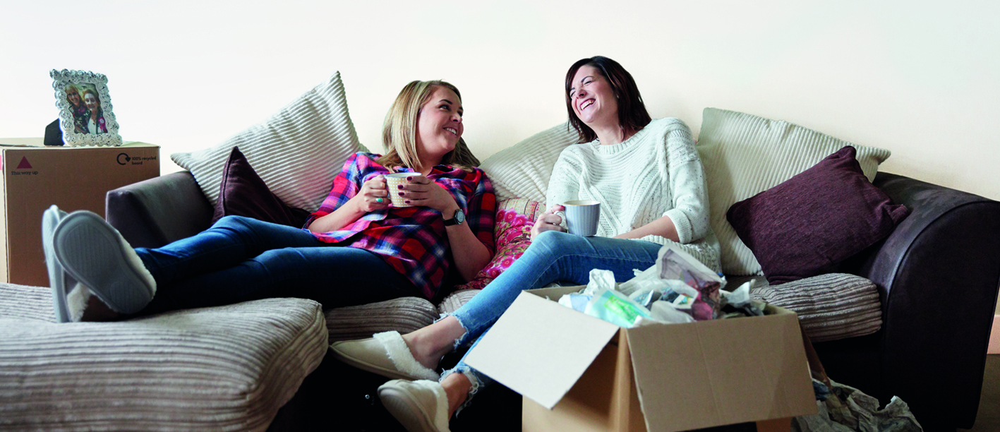 two women sat on a sofa surrounded by moving boxes